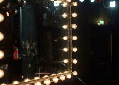 Un miroir de loge de spectacle entourée de lampes allumées.